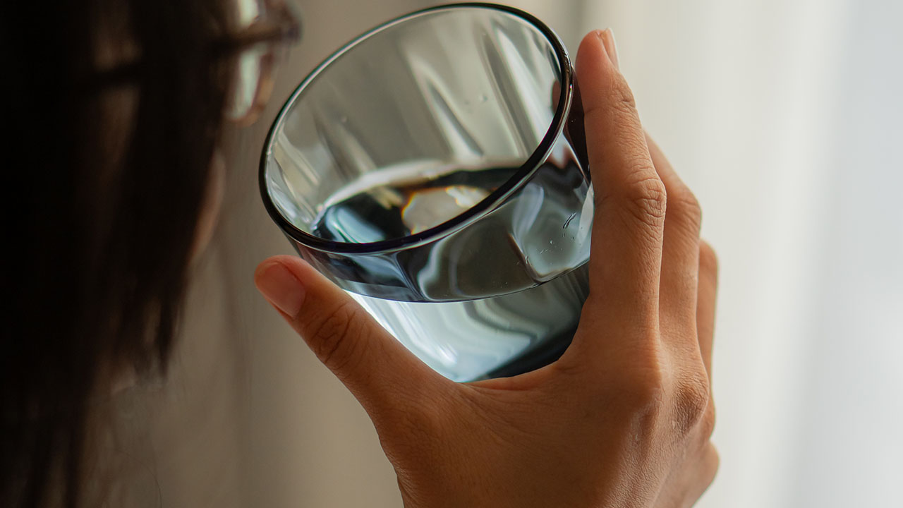 A person, engaging in one of their favorite health hacks, holds a glass of water close to their face.