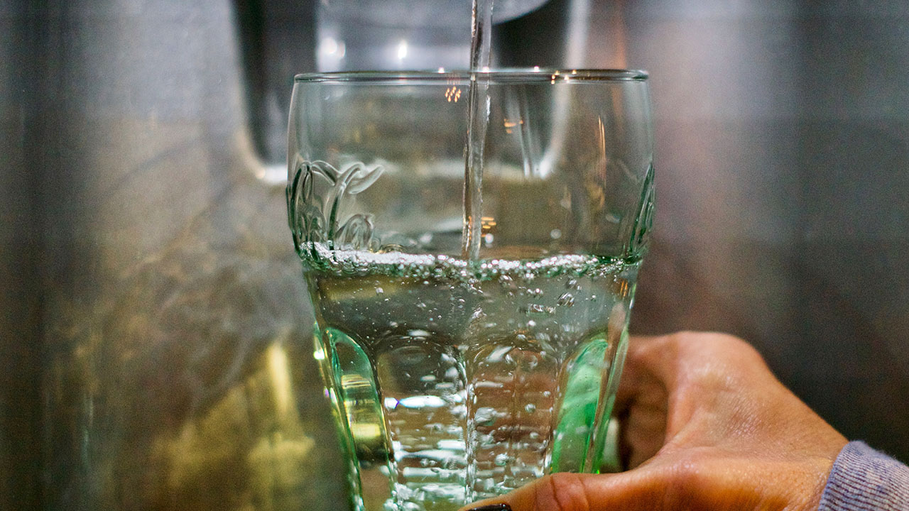 A person is holding a glass under a faucet as water fills the glass, practicing simple health hacks for staying hydrated.