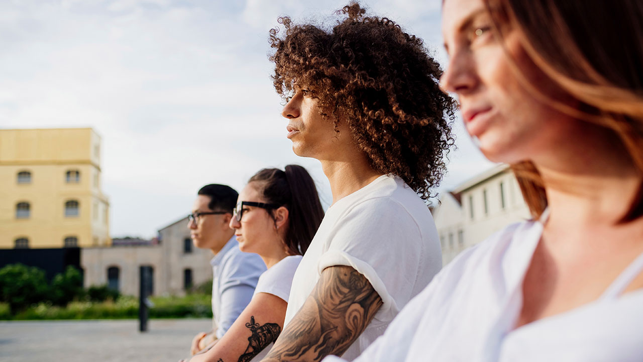 Four individuals stand side by side outdoors, looking into the distance. They are wearing casual clothing and appear focused, perhaps contemplating new health hacks to integrate into their lives.