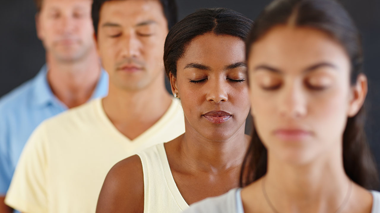 A group of four people, arranged in a line, practice meditation with eyes closed, embracing one of the simplest health hacks for relaxation and mental clarity.