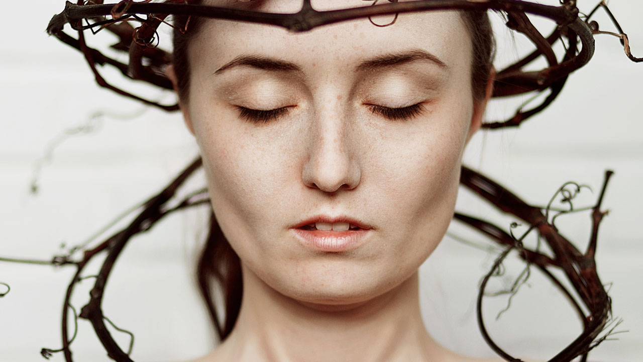 A person with closed eyes is wearing an intricate headpiece made of intertwined branches, offering a serene visual that reflects ancient health hacks for mind and body rejuvenation.