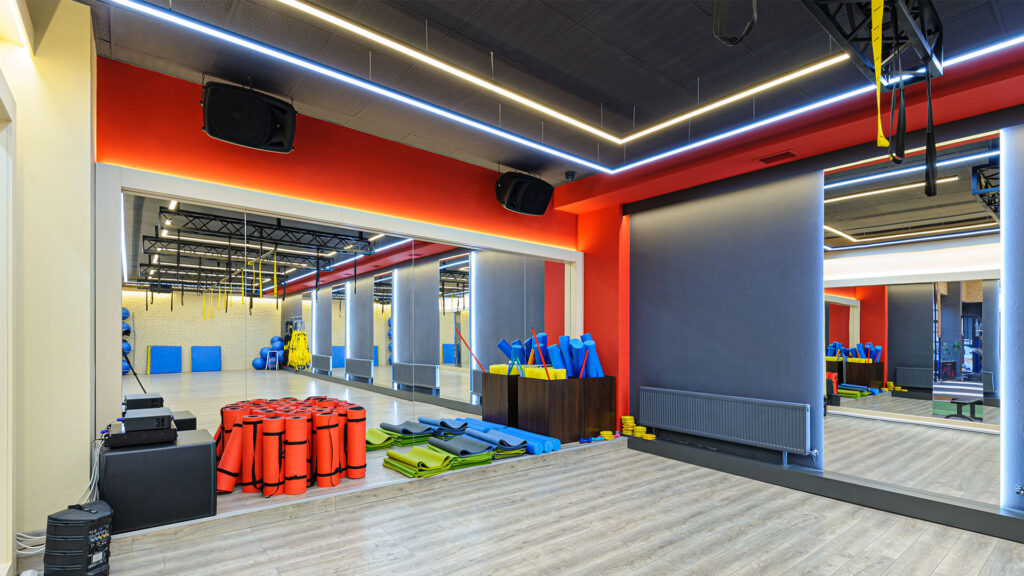 Spacious fitness studio with mirrored walls, stacked yoga mats, foam rollers, and various exercise equipment arranged in an orderly manner—the perfect gym. Bright overhead lighting and modern decor complete the ideal setting for fitness enthusiasts looking for tips and tricks to enhance their workouts.