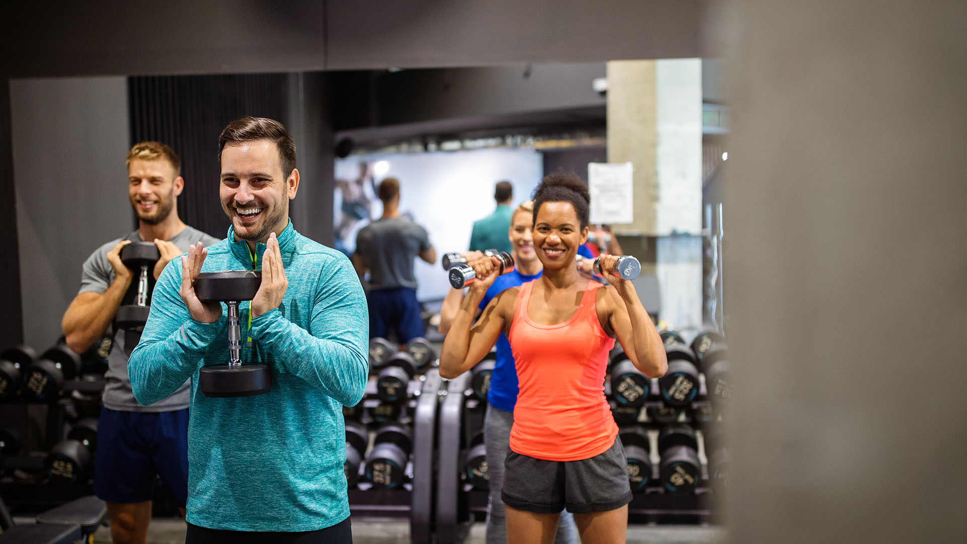 In the perfect gym, a group of people exercise with dumbbells, standing in front of mirrors and workout equipment, learning tips to enhance their workout.